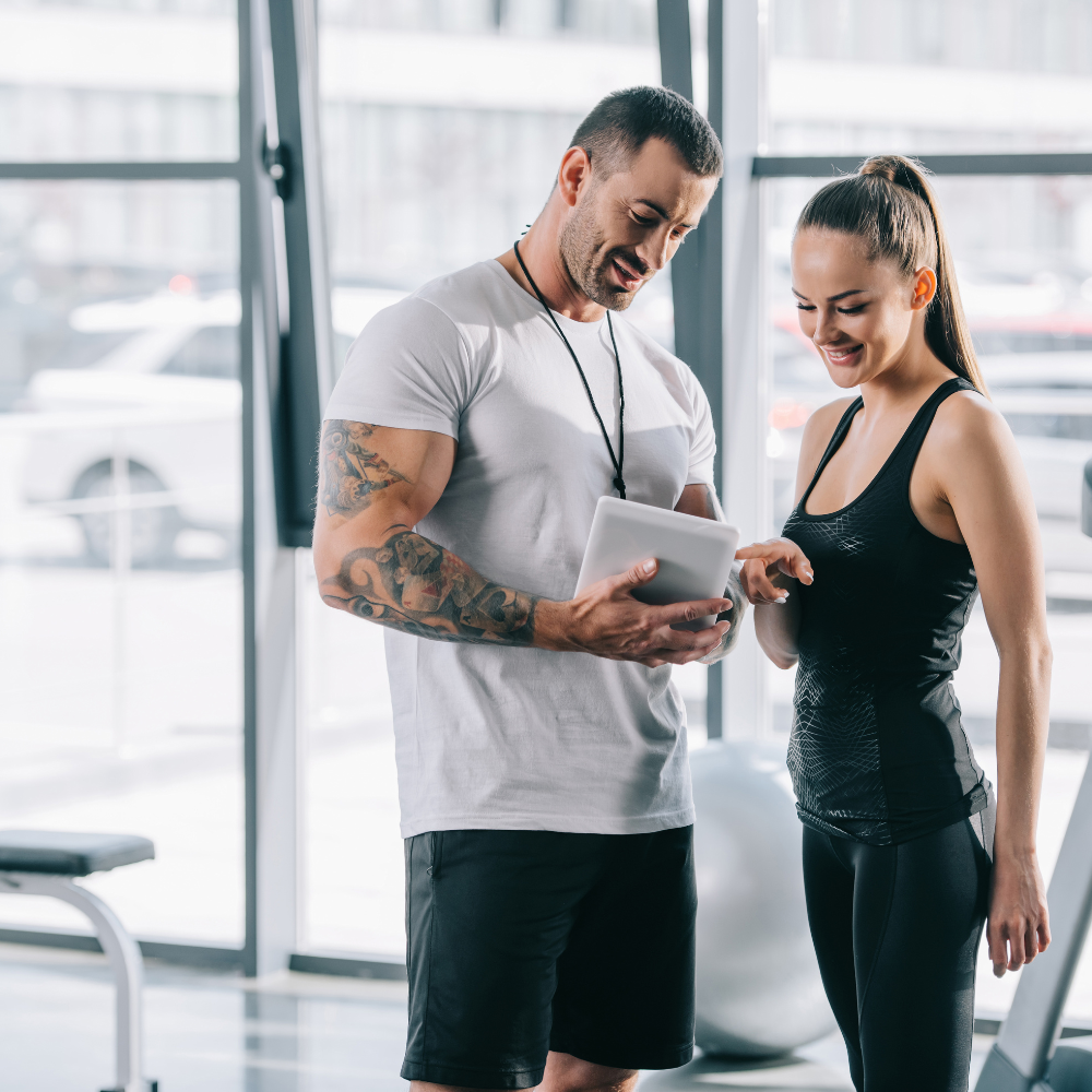 A man and a woman are looking at a tablet in a gym.