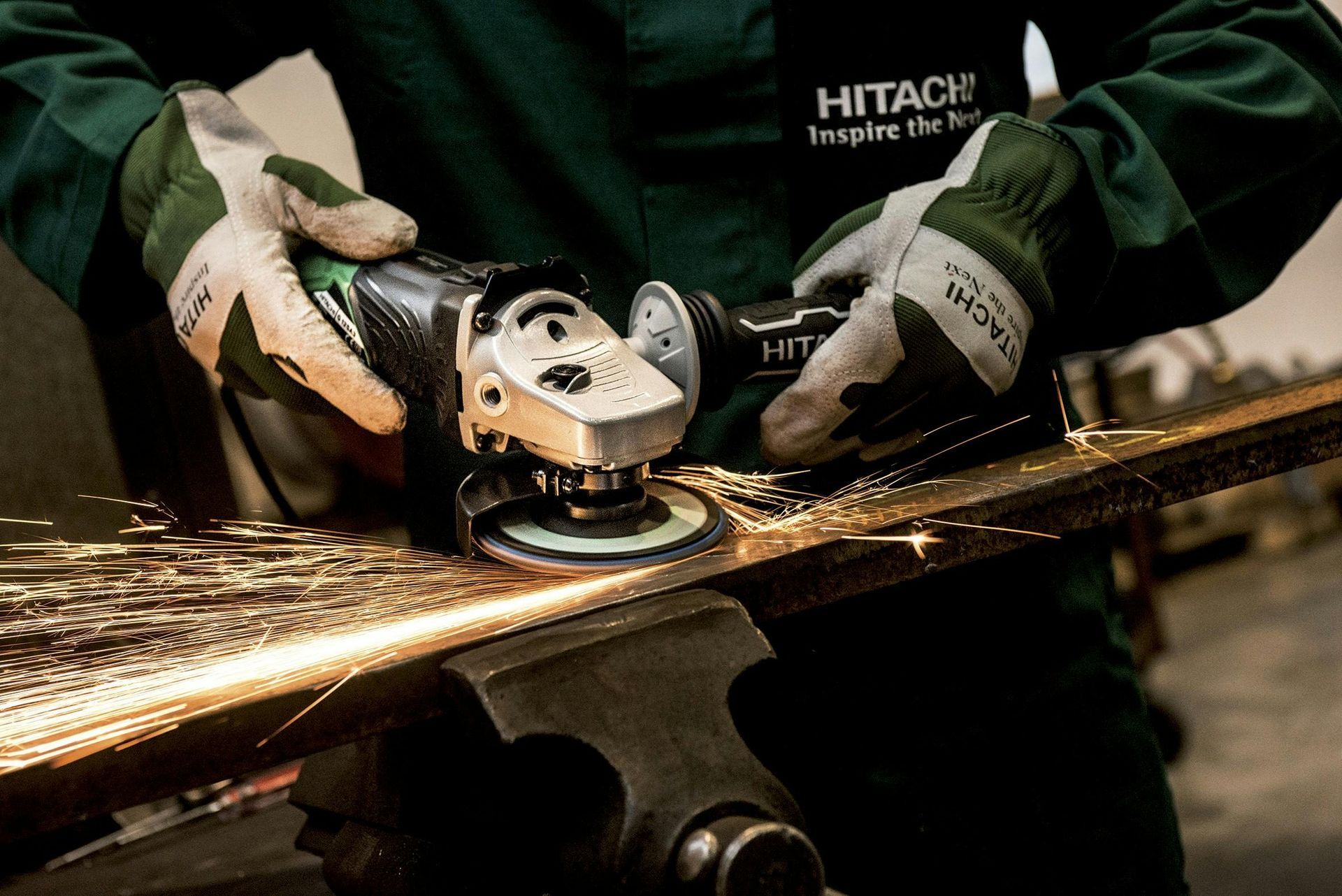Person in work gloves grinding metal with a Hitachi angle grinder, sparks flying.