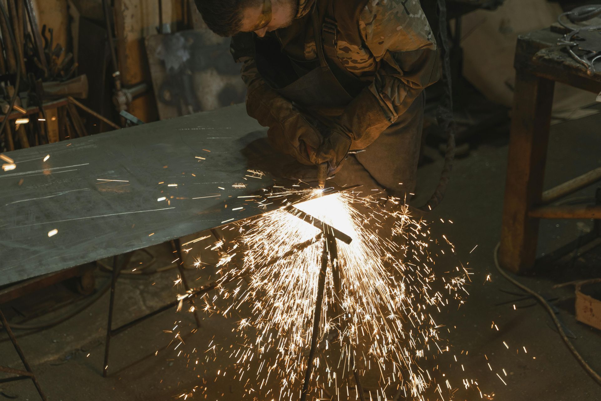 A person using a torch cutter, sparks flying, cutting metal in a workshop.
