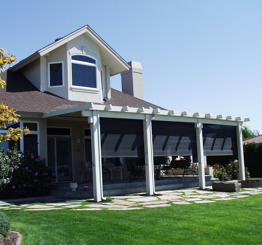 White house with a covered patio and green lawn under a clear blue sky