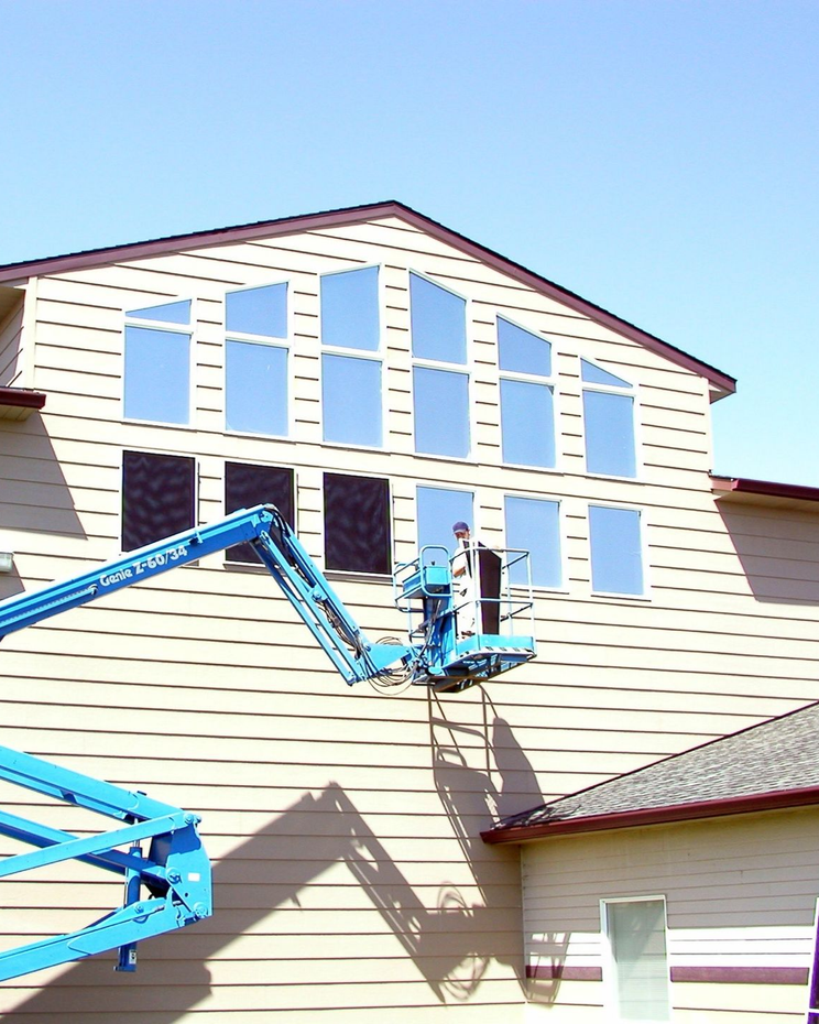 Workers in a blue lift painting a beige house with white shutters and a red roofline