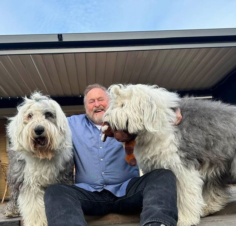 Man sitting with two large shaggy dogs under a porch roof
