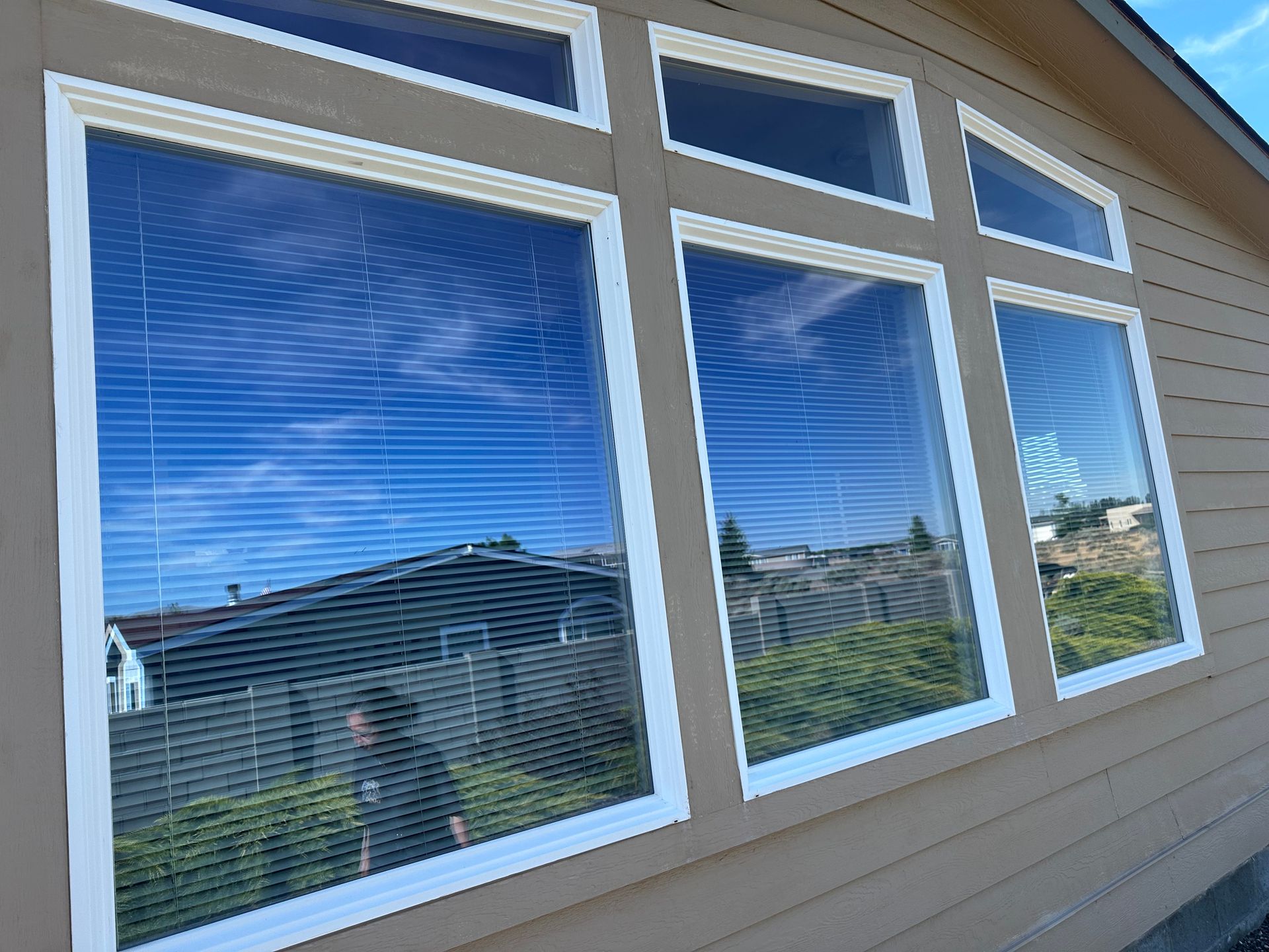 White-framed windows reflecting blue sky on a tan house exterior