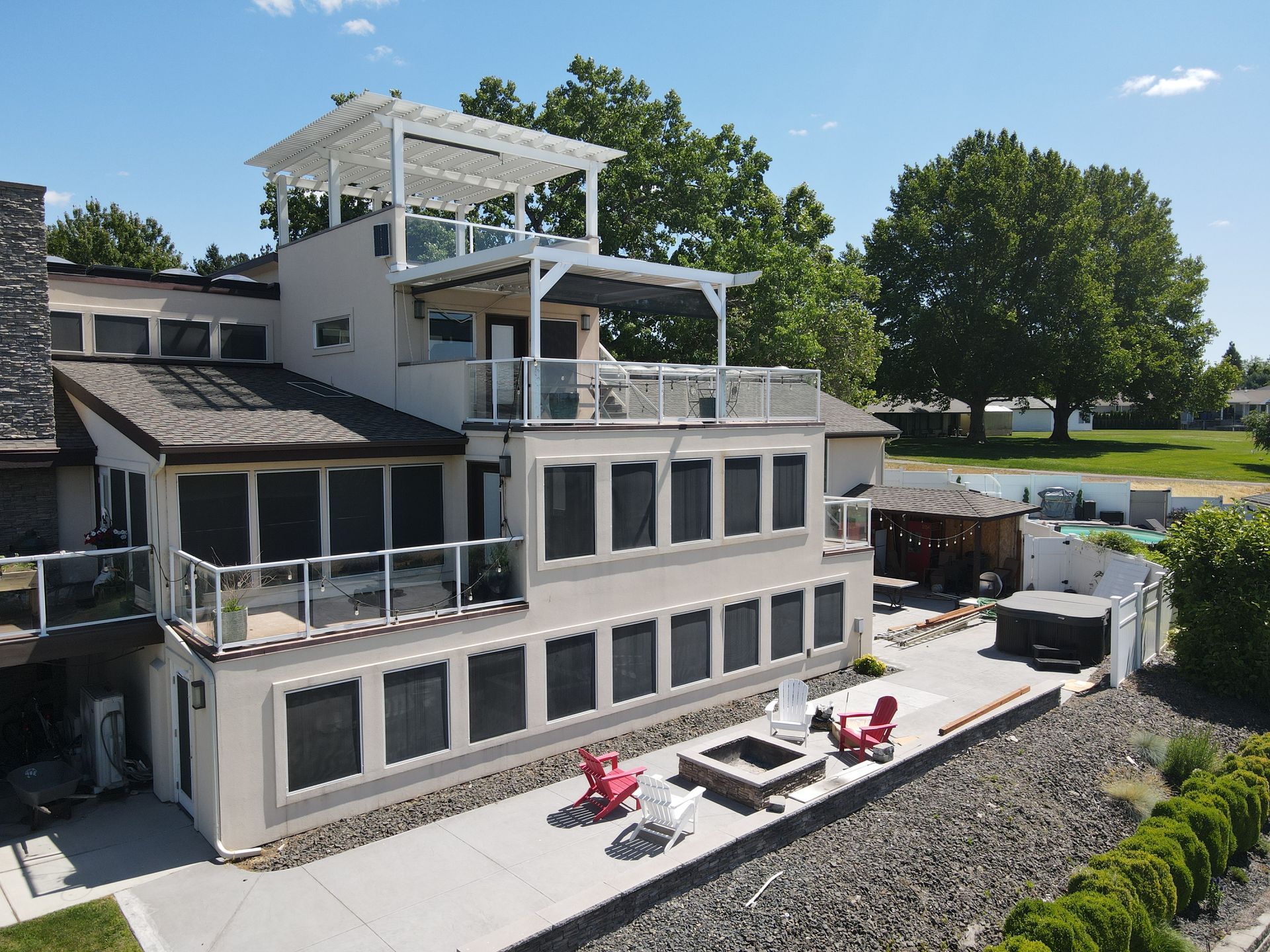 Modern white lakeside house with decks, patio chairs, and a rocky shoreline under clear skies