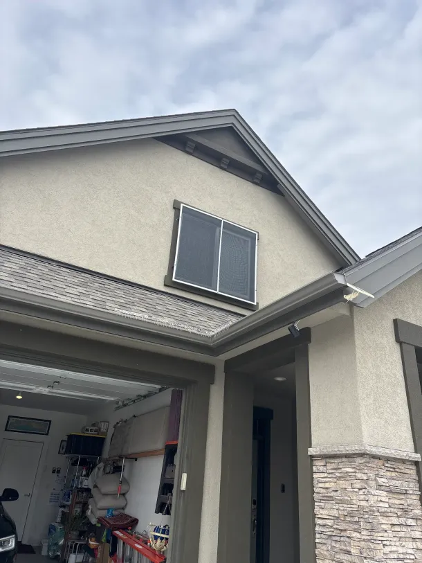Two-story beige house with an open garage and dark-framed upper window under a cloudy sky