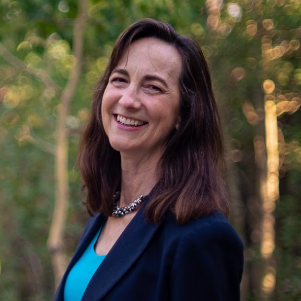 a woman in a blue shirt and jacket is smiling in front of trees .