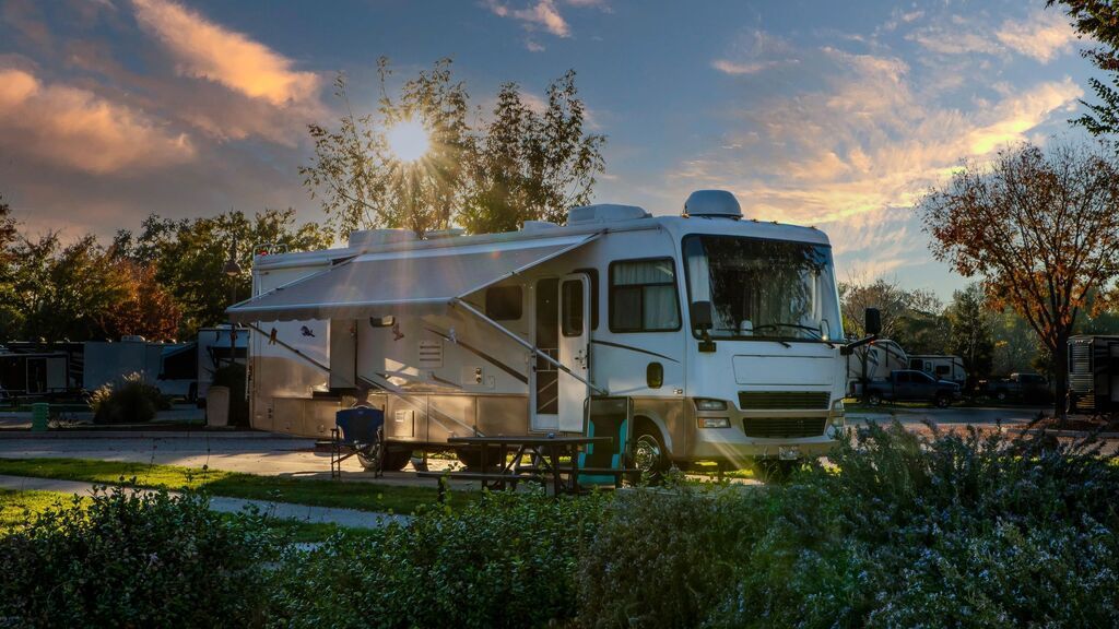 White RV parked at a campsite at sunset, with trees and orange clouds in the background.