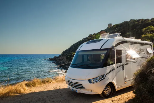RV parked in a golden field at sunrise, with misty hills and trees in the background