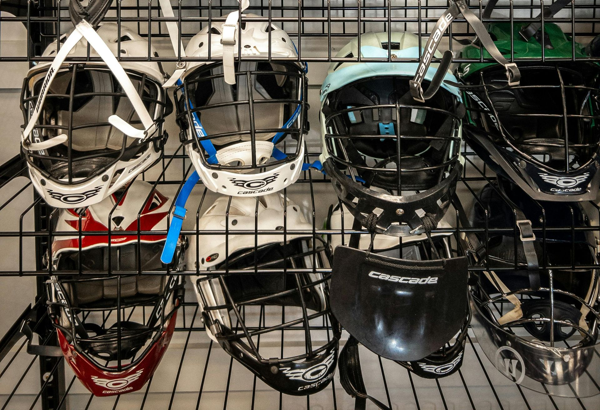 Lacrosse goalie helmets and face masks displayed on a store rack.