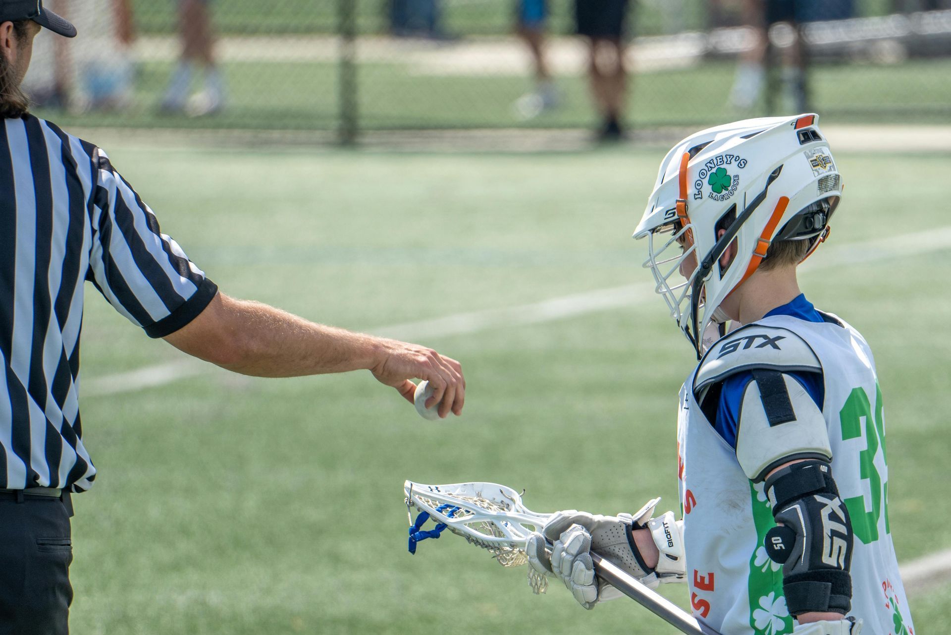 Referee and youth lacrosse player on a field, with the referee pointing during play