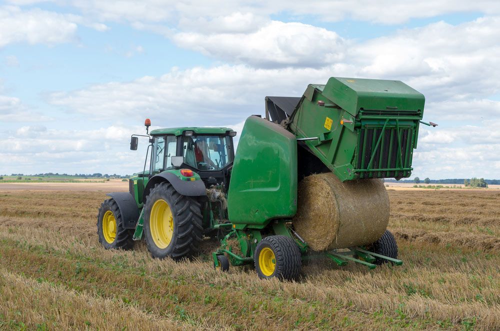 Harvesting Scene: Round Baler Discharging Fresh Wheat Bale — Thompson's Farm Gear In Port Macquarie, NSW