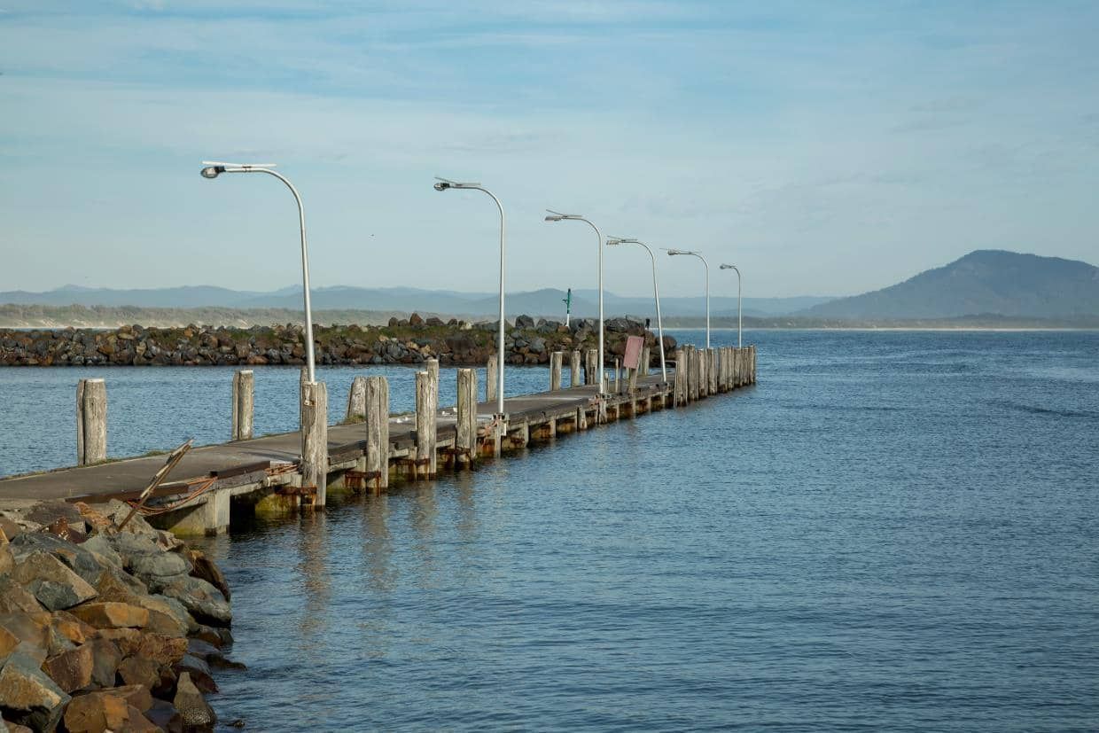 A Dock Leading Into a Body of Water with Mountains in The Background — Thompson's Farm Gear In Taree, NSW