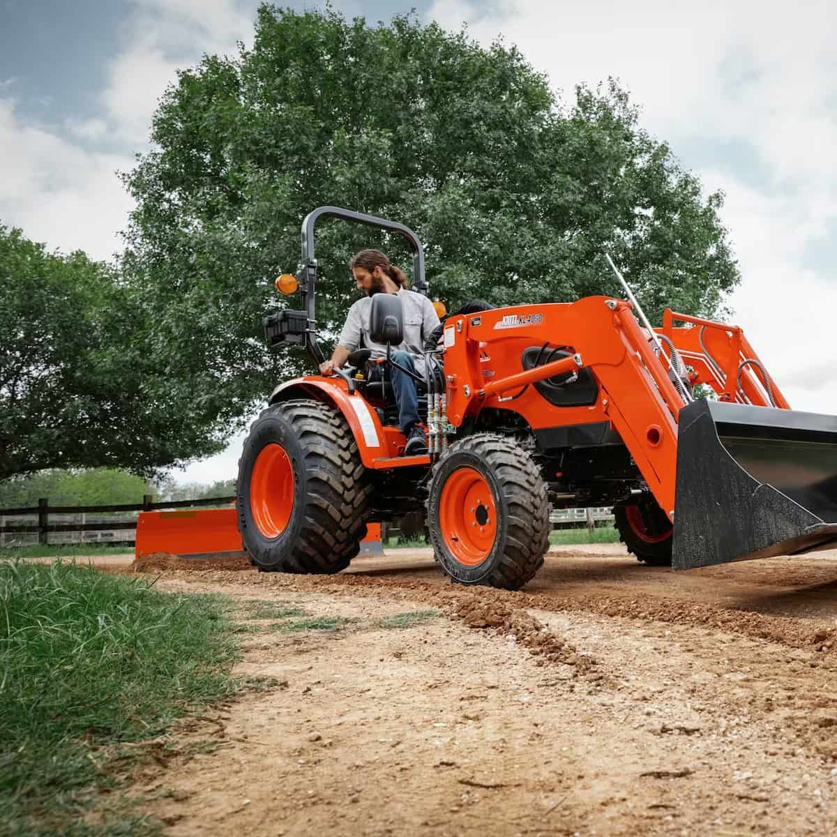 Orange Tractor With Front Loader Driving On A Dirt Path — Thompson's Farm Gear In Wauchope, NSW