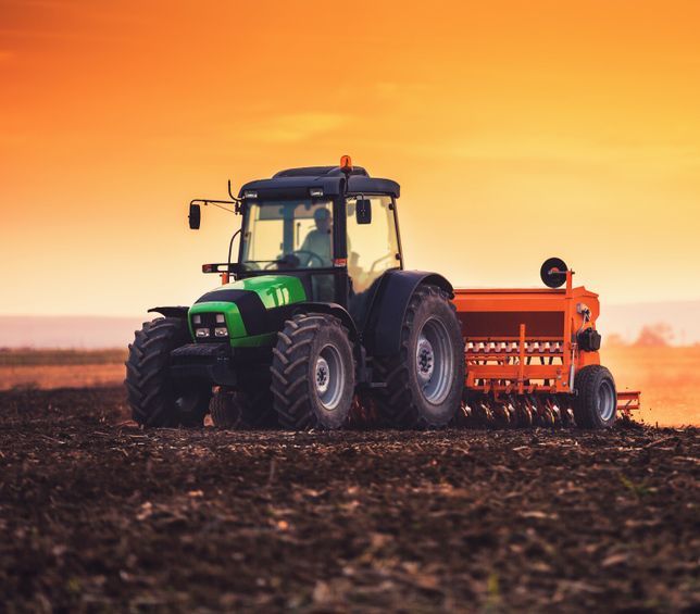 Farmer Seeding a Field with Tractor at Sunset — Thompson's Farm Gear In Port Macquarie, NSW