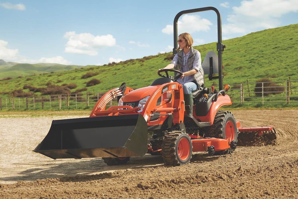 Person Driving An Orange Tractor With A Front Loader And Rear Mower — Thompson's Farm Gear In Wauchope, NSW