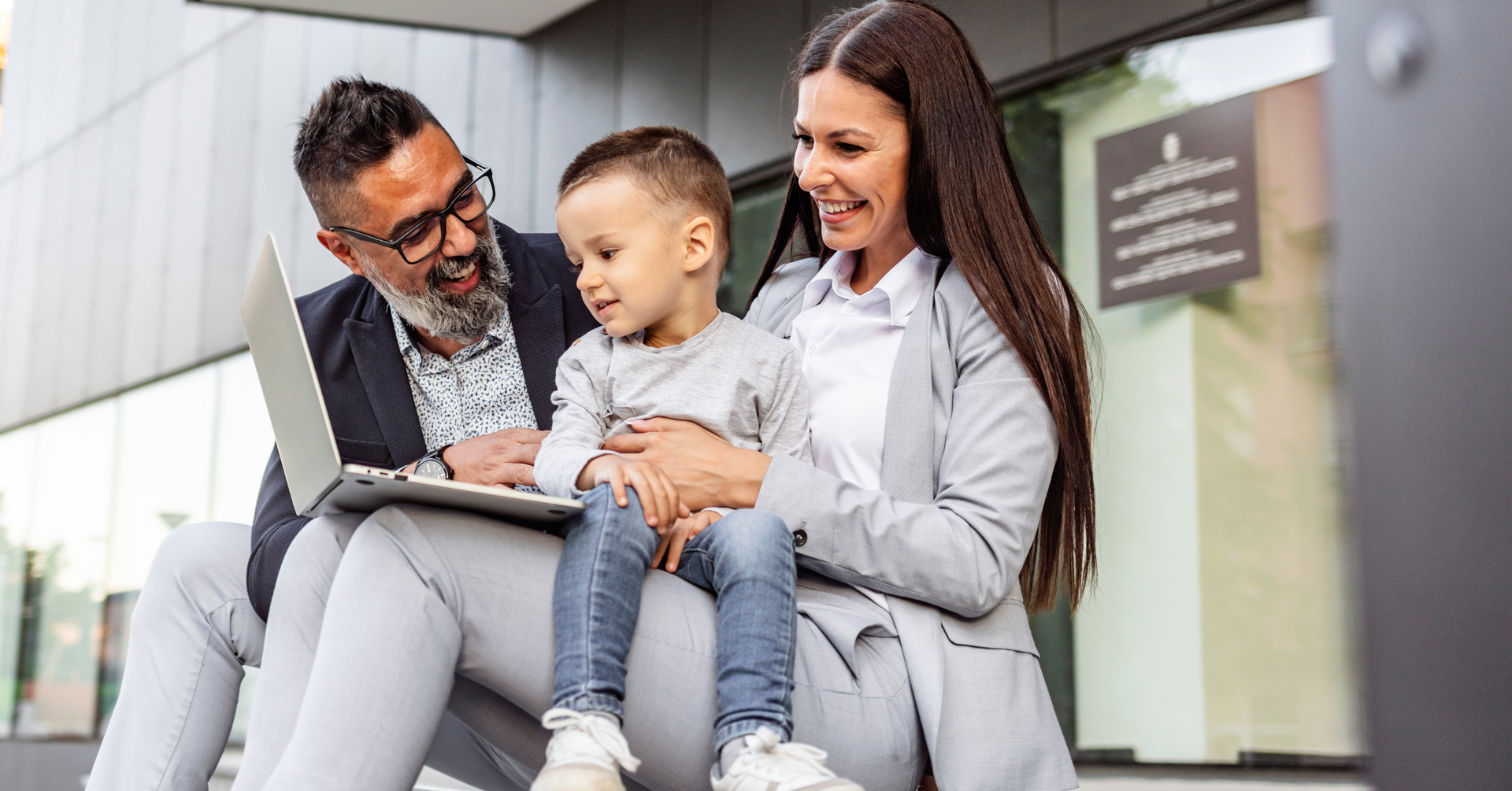 A family is sitting on a bench looking at a laptop.
