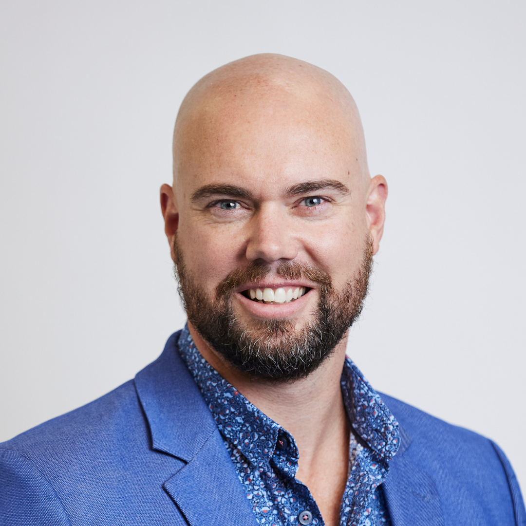 A bald man with a beard is wearing a blue suit and smiling.