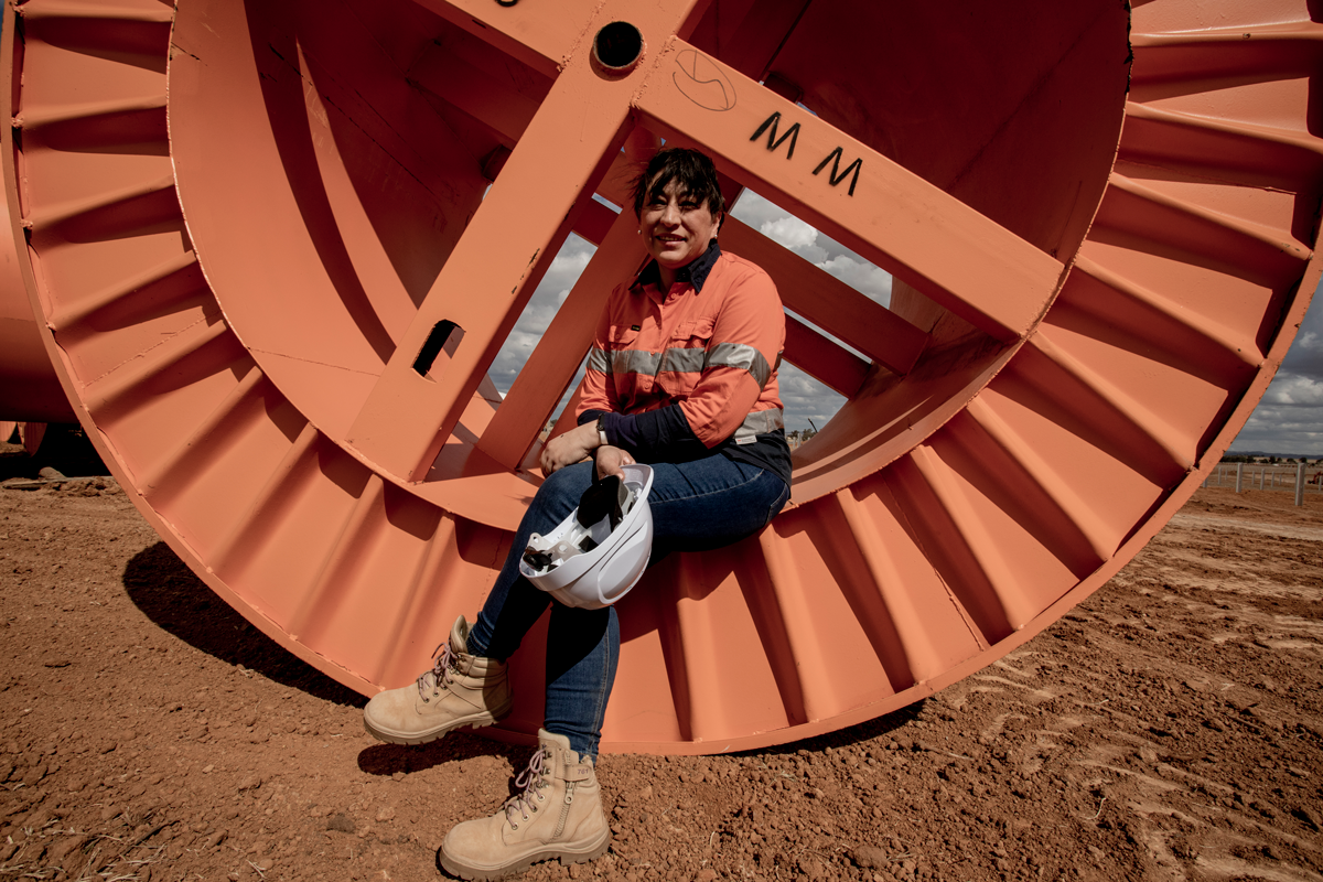 A woman is sitting on a large orange spool holding a helmet.