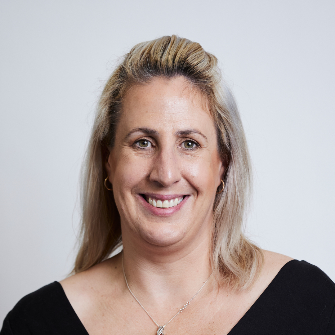 A woman wearing a black shirt and a necklace is smiling for the camera.