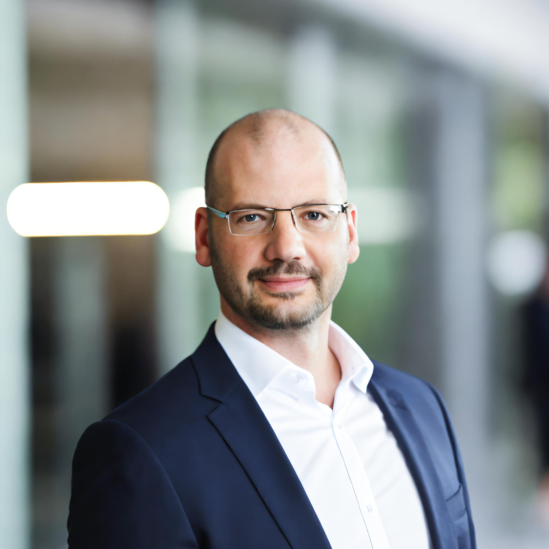A man in a suit and glasses is smiling for the camera