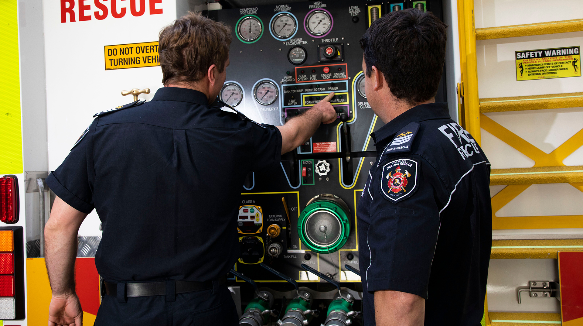 Two firefighters are looking at a control panel on a fire truck.