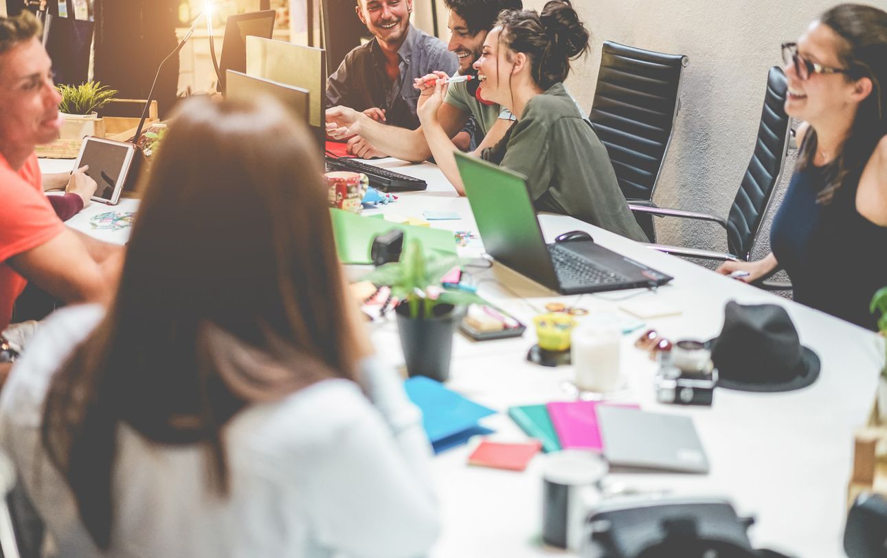 People collaborating around a table with laptops, notebooks, and coffee in a bright meeting room