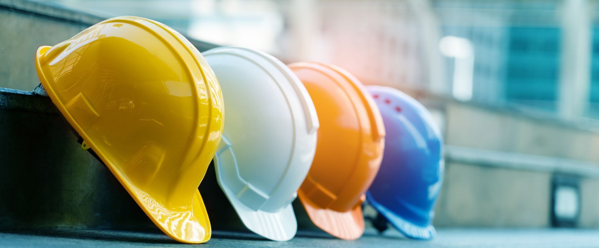 Three hard hats in yellow, white, orange, and blue lined up on a surface outdoors