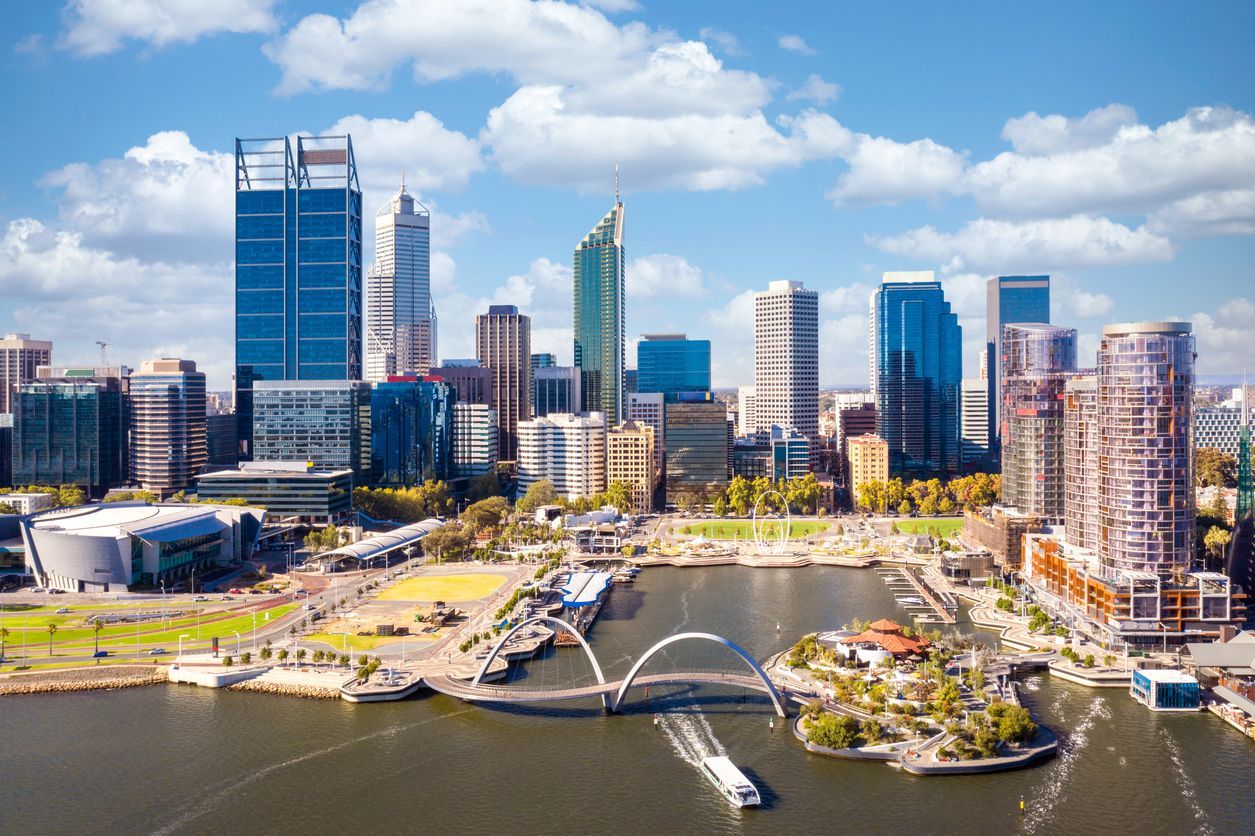 Waterfront city skyline with modern buildings, a bridge, and a marina under a blue sky