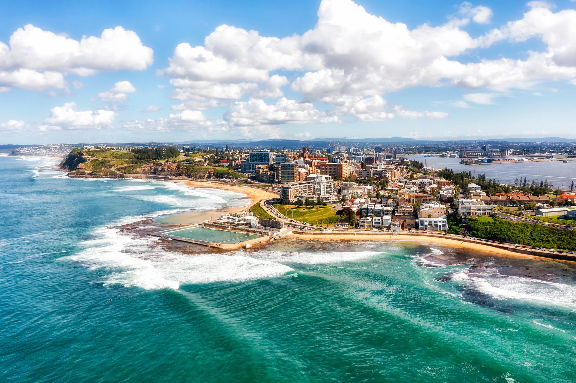 Aerial view of a coastal city with turquoise water, sandy beaches, and a cloudy blue sky