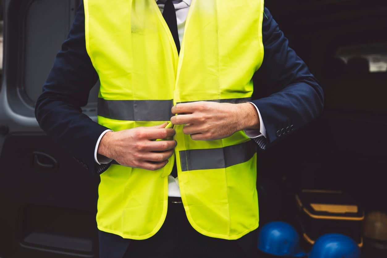 Man in suit zipping up a bright yellow safety vest, standing near a car.