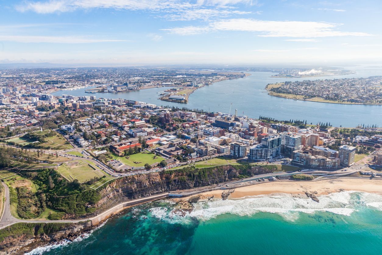 Aerial view of a Newcastle with beaches, harbor, and turquoise ocean under a clear sky