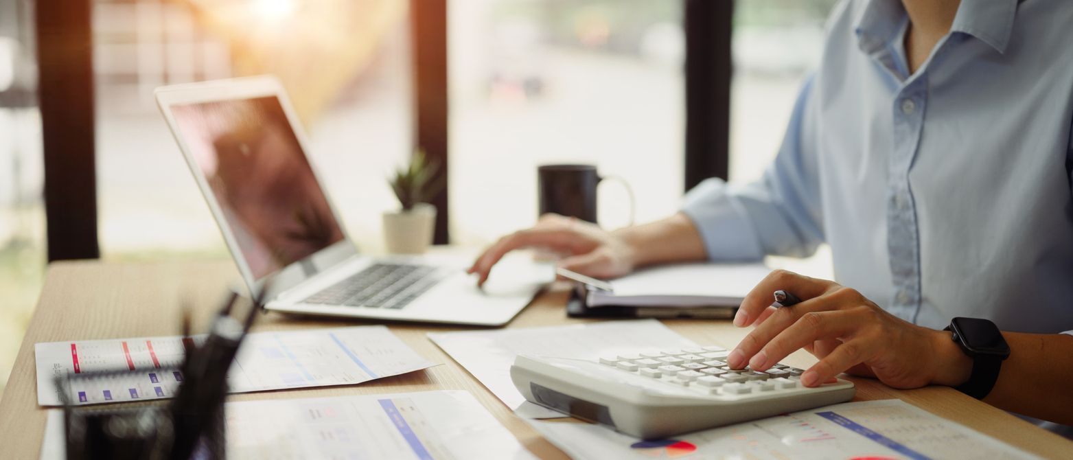 Person working at a desk with a laptop, papers, and a calculator in a bright office