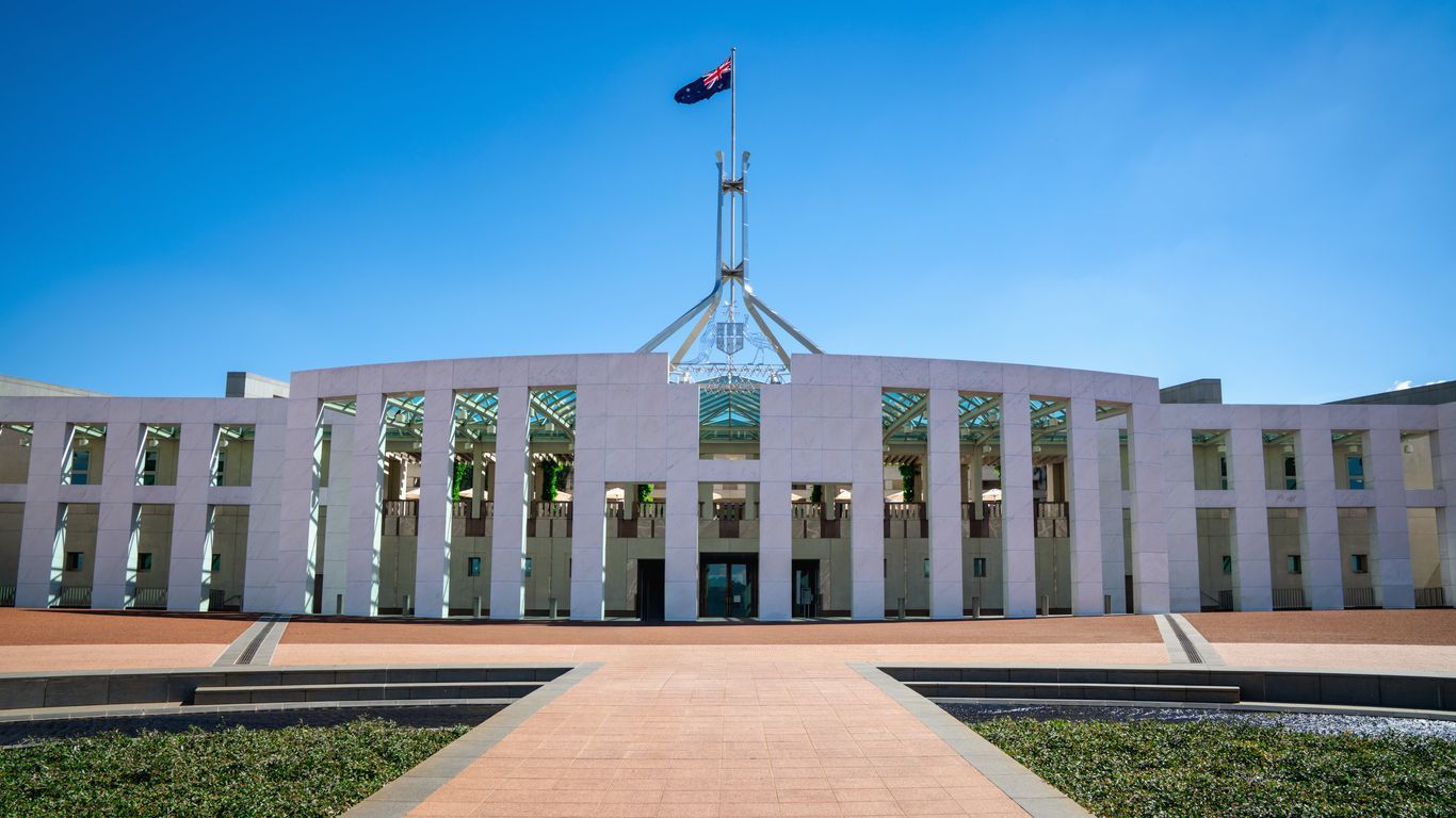 Australian Parliament House with central flag, viewed from a walkway under a clear blue sky