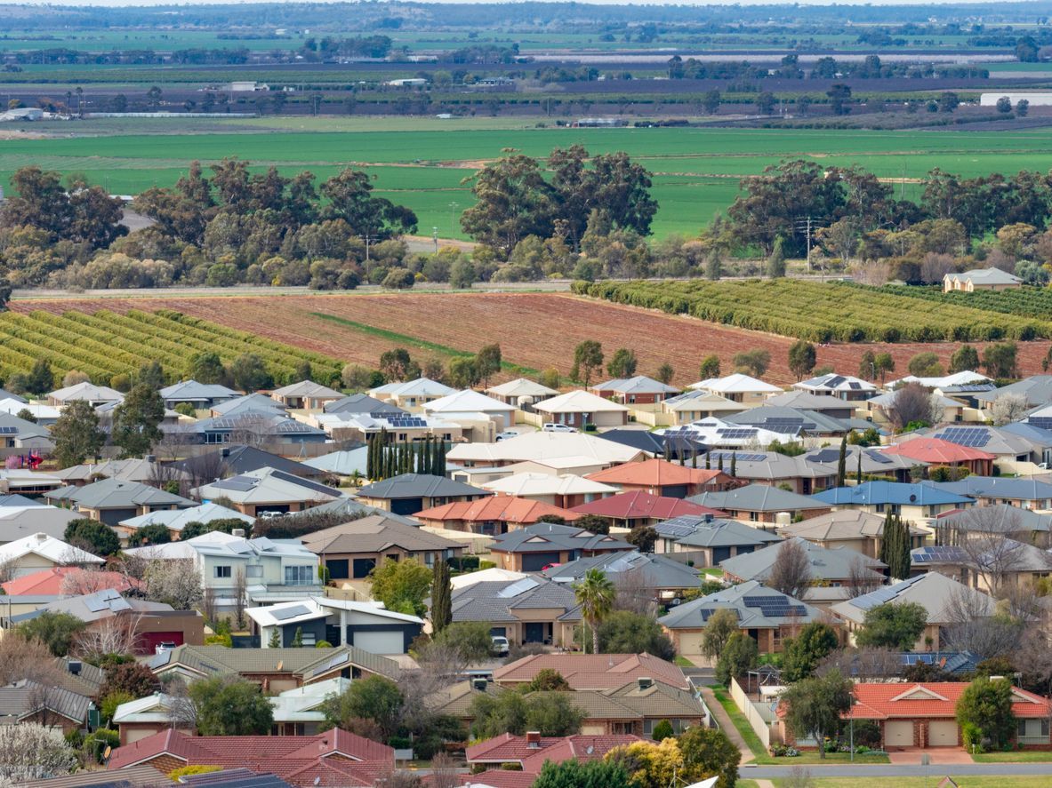 Suburban neighborhood with colorful rooftops beside fields and trees under a clear sky