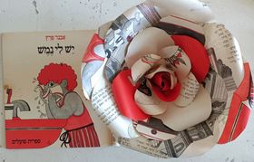 פרח נייר עם דפים אדומים ולבנים לצד כריכת ספר מאוירת עם טקסט עברי