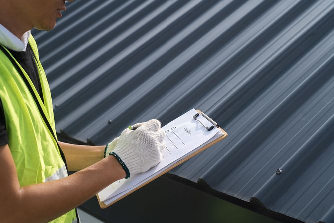 Worker in a high-visibility vest inspecting a corrugated metal roof with a clipboard.