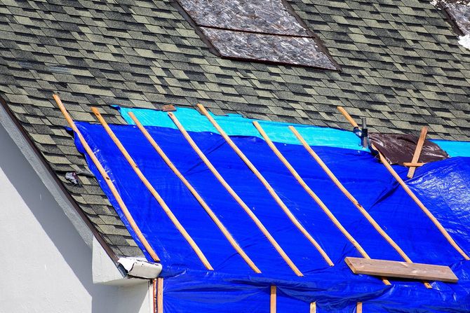 Blue tarp and wooden slats secured over part of a shingled roof for repairs