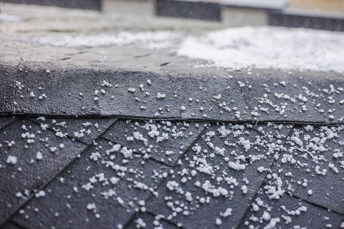 Hailstones scattered across a dark shingled roof after a hailstorm