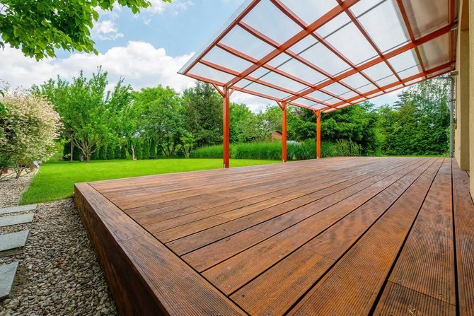 Wooden deck with metal pergola in a green garden, viewed from a low angle