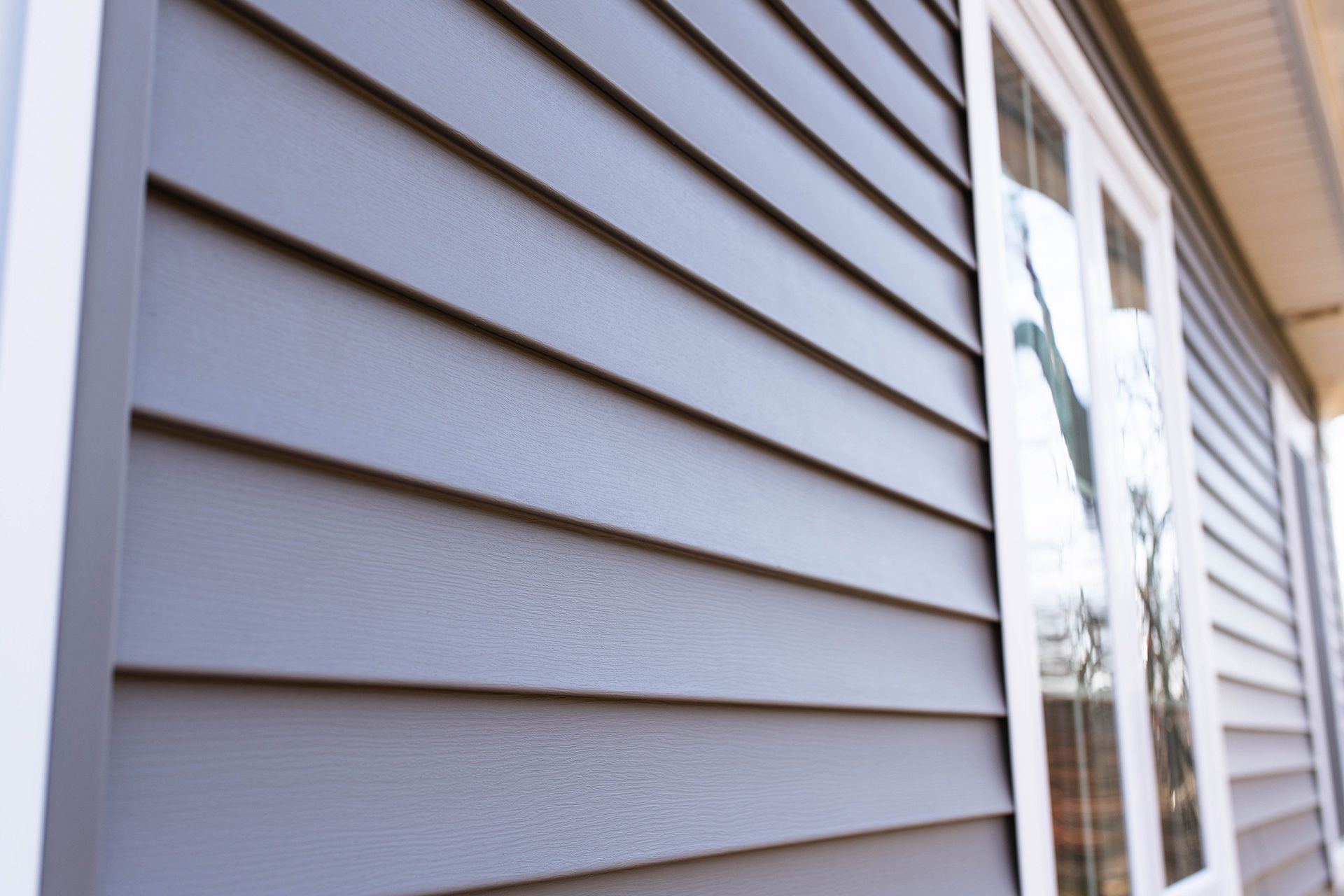 Close-up of gray vinyl siding on a house exterior beside a window and roofline.