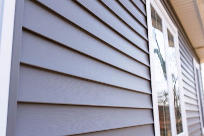 Close-up of gray vinyl house siding beside a window reflection