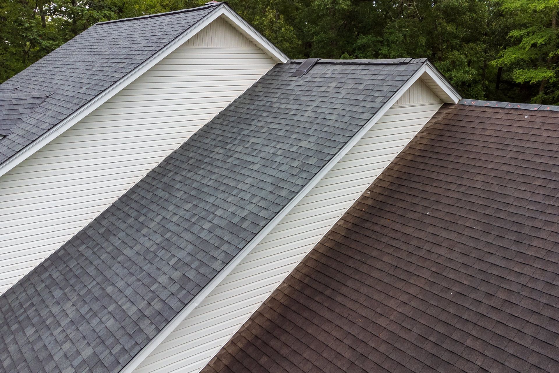 Three adjacent house roofs in white, gray, and brown shingles viewed from above.