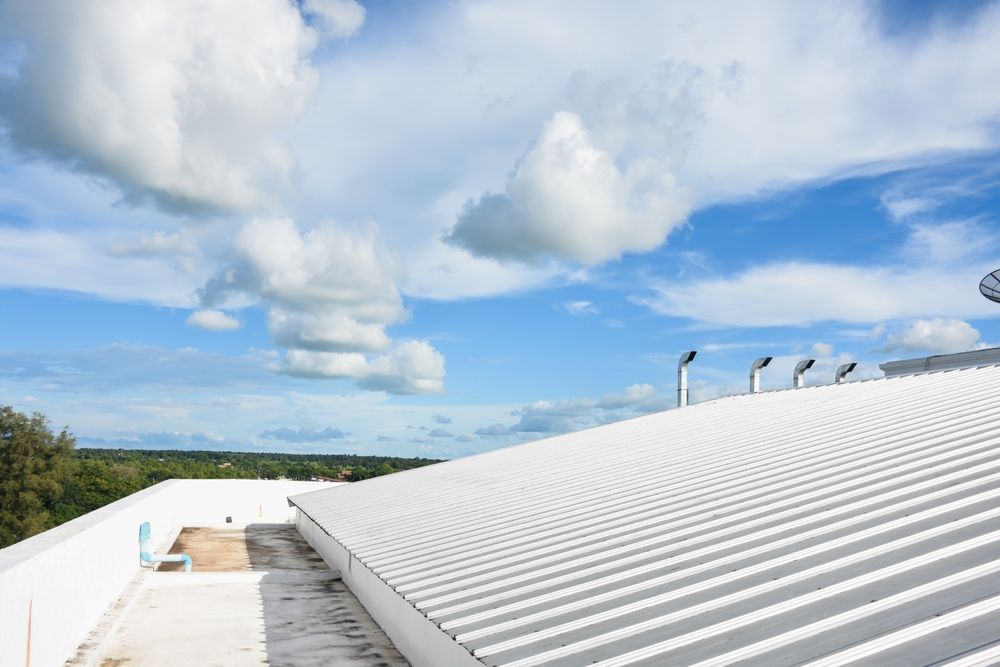 White corrugated roof under a blue sky with clouds and distant trees