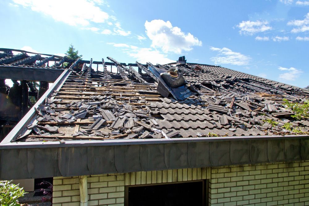 Partially collapsed roof with missing shingles on a damaged building under a blue sky