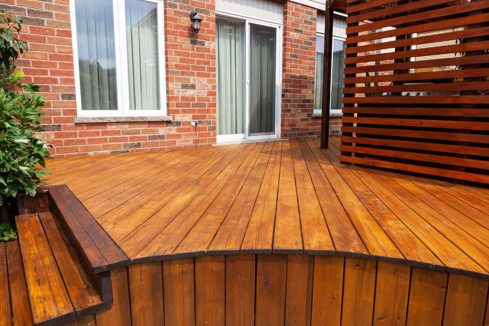 Wooden backyard deck beside a red brick house with a white sliding door and horizontal privacy screen