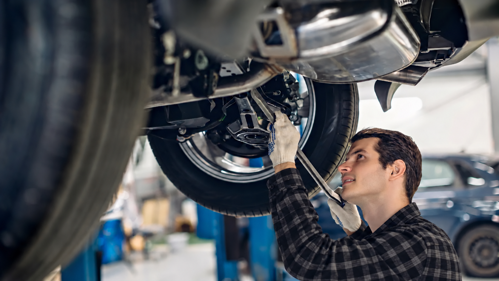 Mechanic in red uniform inspecting a car’s undercarriage in an auto repair shop