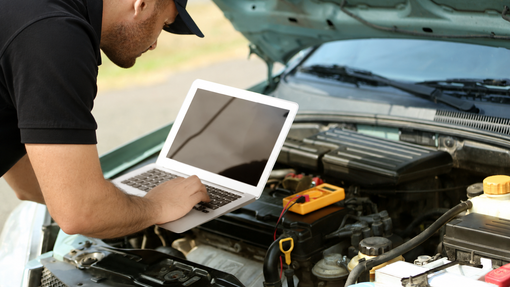 Mechanic in red uniform using a laptop to diagnose a car engine in an auto shop
