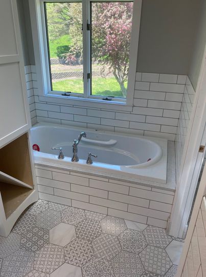 Small bathroom with a white clawfoot tub, subway tile wall, and window overlooking a garden.