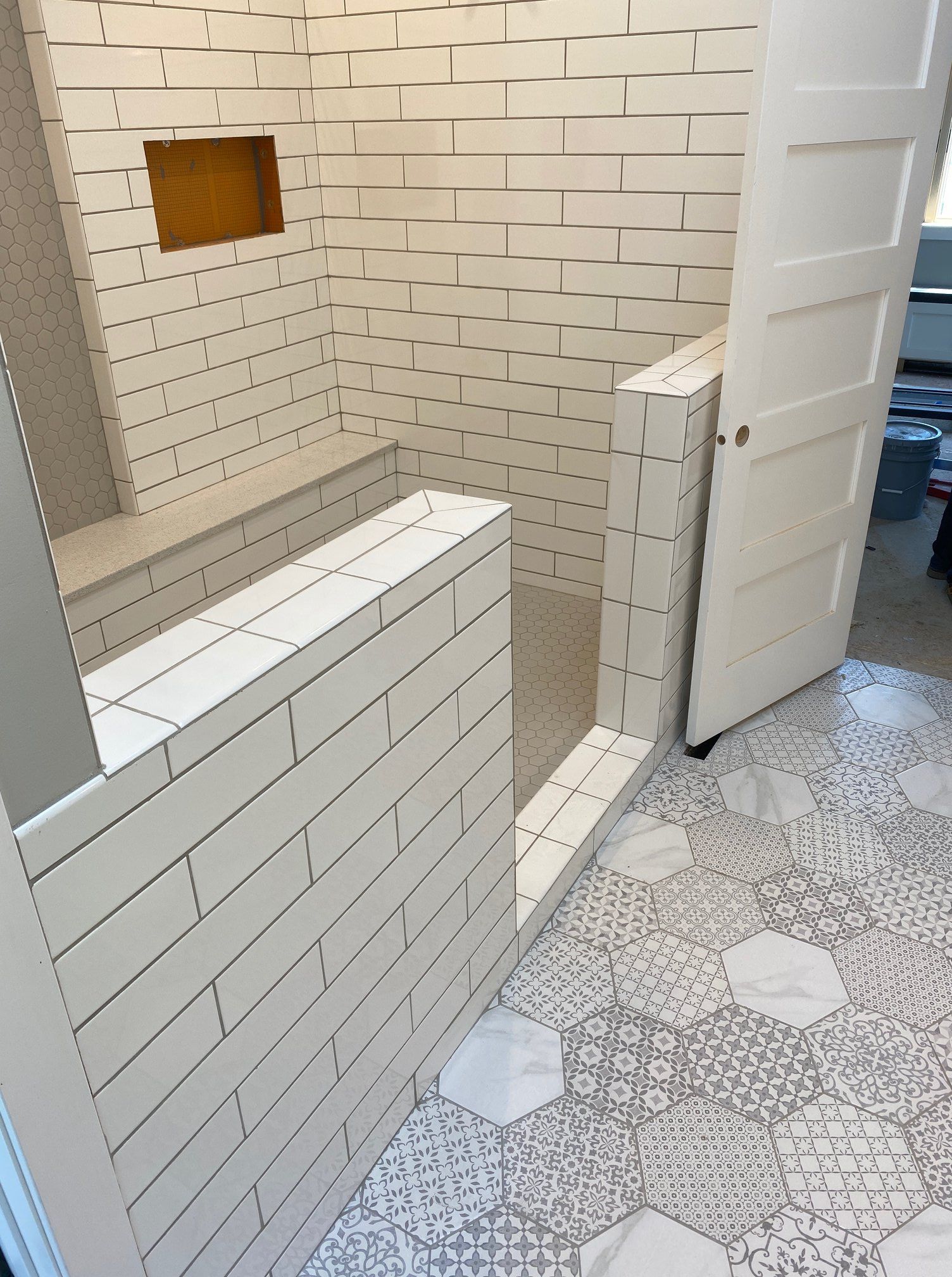 White-tiled restroom partition and open stall door on patterned tile floor