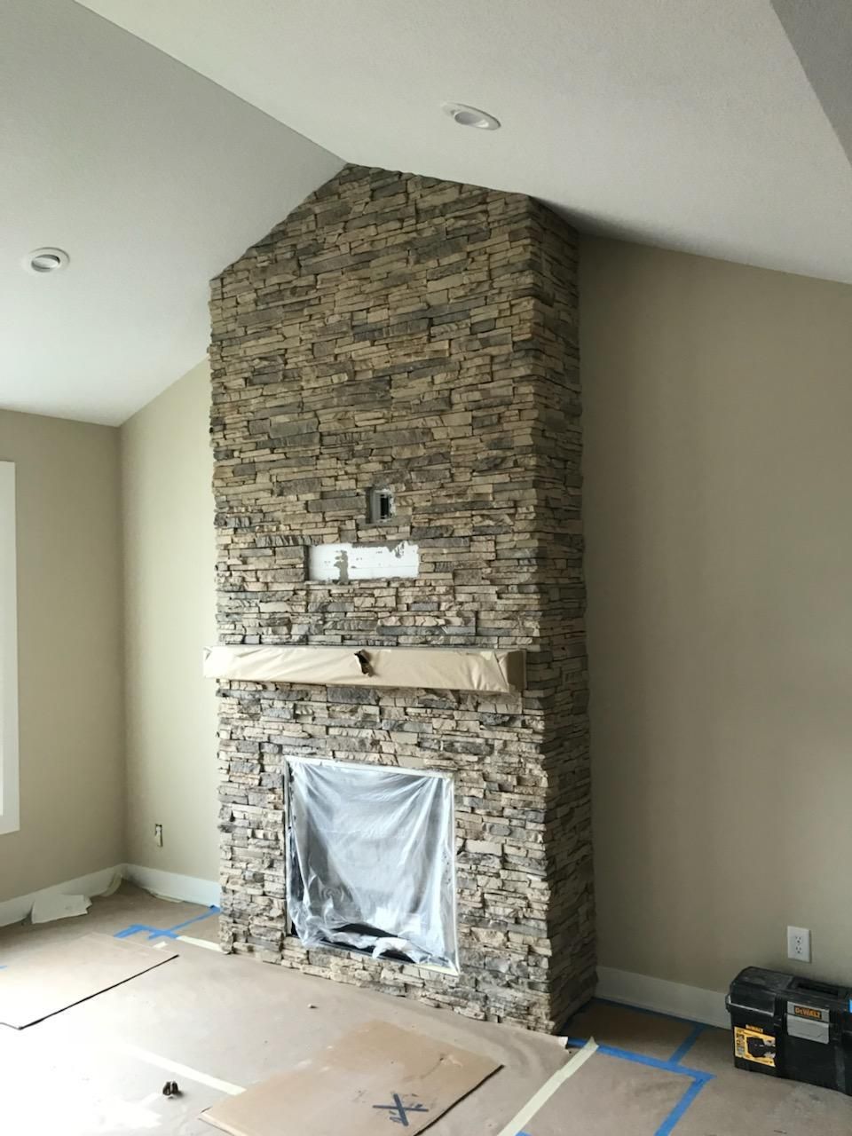 Stone fireplace under construction in a beige room with a framed opening and unfinished floor